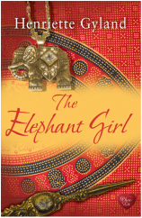 Book cover for The Elephant Girl by Henriette Gyland, a book edited by Romance Refined editor Rachel Daven Skinner. Book cover shows an Indian-style elephant pendant set atop an Indian-patterned cloth
